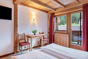 Una habitación de madera con cama, una mesa con sillas, un televisor y una ventana con cortinas.