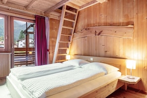Une chambre aménagée dans une cabane en bois, avec un lit, une échelle et une table de chevet dotée d’une lampe.