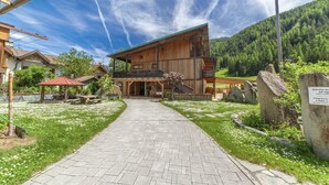 Ein Holzhaus mit Balkon, einem gepflasterten Weg und einer Bergkulisse.