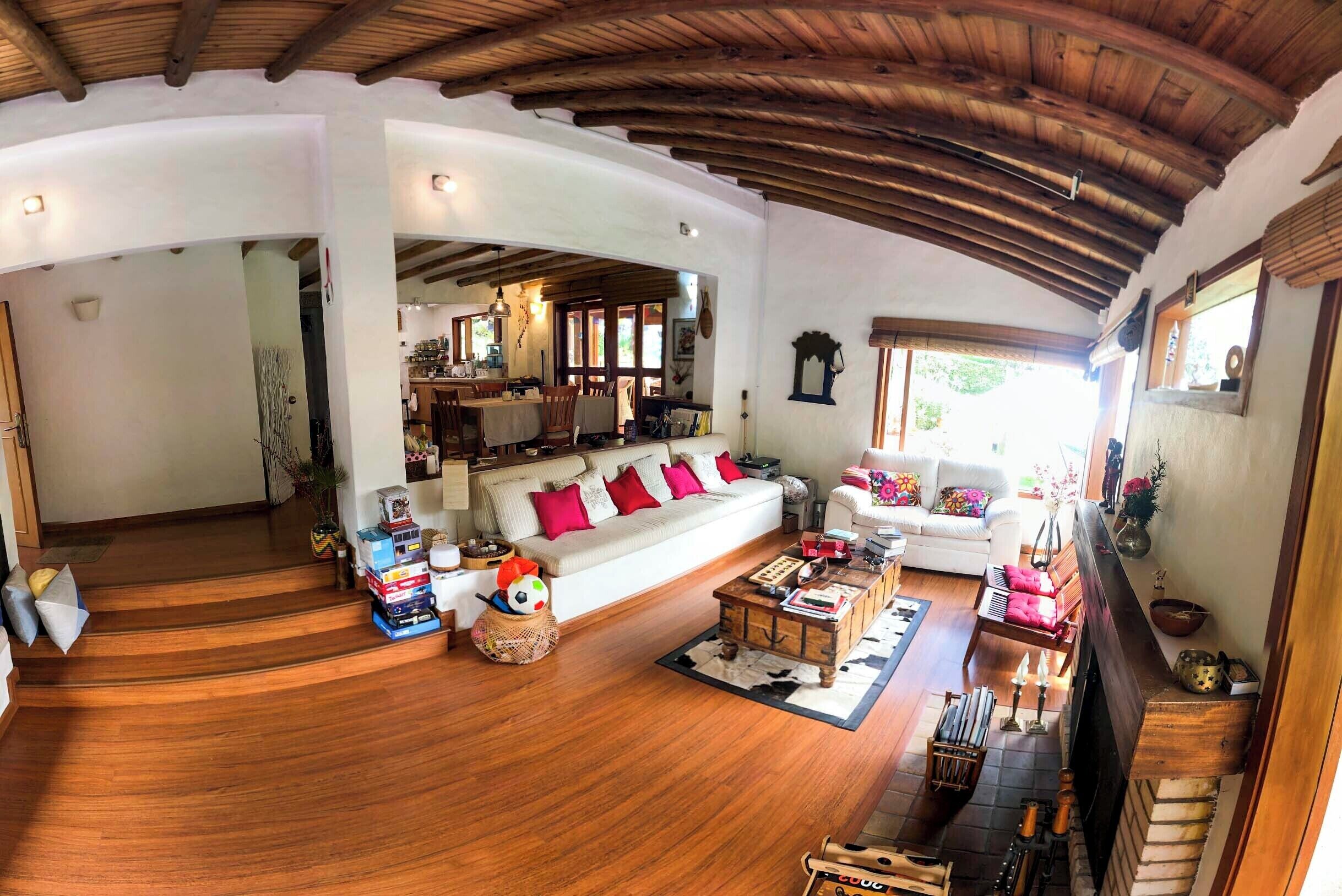 A spacious living area with a wooden ceiling, a sofa with red cushions, a coffee table, and a fireplace.