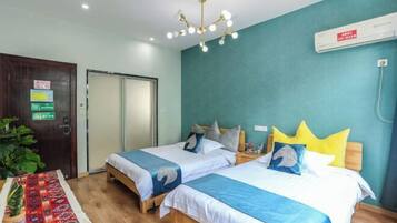 Una habitación de hotel con dos camas, suelo de madera, pared color verde azulado y una lámpara en el techo.