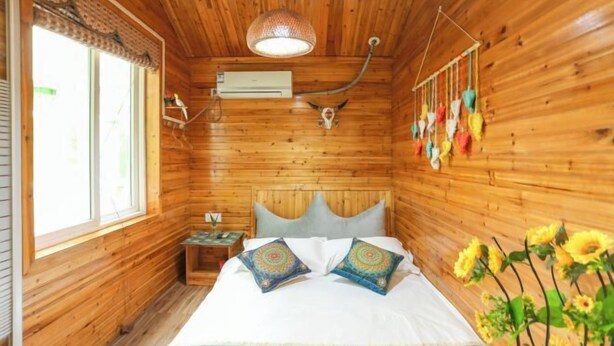 Un dormitorio tipo cabaña de madera con cama, almohadas, una lámpara colgante, un equipo de aire acondicionado y una ventana.