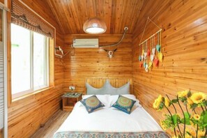 A wooden cabin bedroom with a bed, pillows, a hanging light fixture, an air conditioning unit, and a window. - Moshang Huakai Inn (Tongxiang)