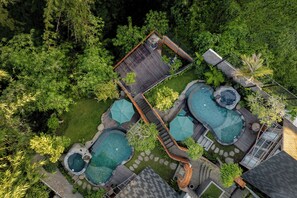 Ett flygbildsfoto av en bostadsfastighet med flera pooler, ett trädäck och frodig grönska.