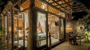 A cozy, well-lit wooden cabin with a bed, a small table, and a seating area. - Agastya Ubud Villa (Ubud)