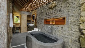 A stone-walled bathroom with a freestanding bathtub, wooden shelves, and a wooden ceiling. - Agastya Ubud Villa (Ubud)