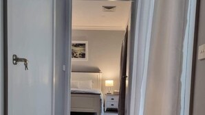 A narrow hallway leading to a bedroom with a bed, nightstand, and a lamp. - 229 - The Pool House (South Albury)