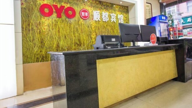 Ein Empfangstresen mit digitalem Bildschirm und Kassenterminal vor einer Wand mit dekorativem Design und der Aufschrift "OYO" und "顺都宾馆".
