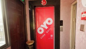 Ein roter Aufzug mit dem OYO-Logo, einem hölzernen Hocker und einer Tür mit floralem Muster.