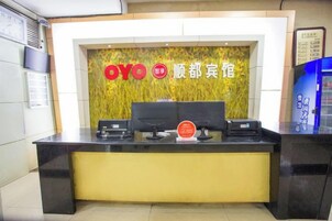 Un mostrador de recepción con una encimera negra y una base amarilla, un cartel rojo y blanco encima, y una pared con diseño decorativo.