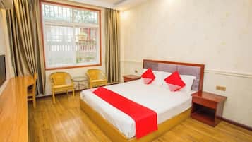 Habitación de hotel con una cama grande, un escritorio, dos sillas, una mesita y una ventana con cortinas.