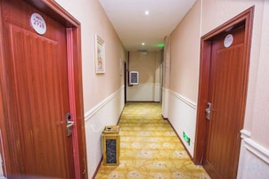 A hotel corridor with wooden doors, a patterned carpet, and a small trash bin.