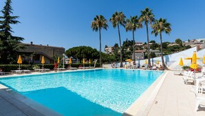 Une piscine d’un bleu éclatant, bordée de chaises longues blanches et agrémentée de parasols jaunes, le tout entouré de palmiers et avec des bâtiments en arrière-plan.