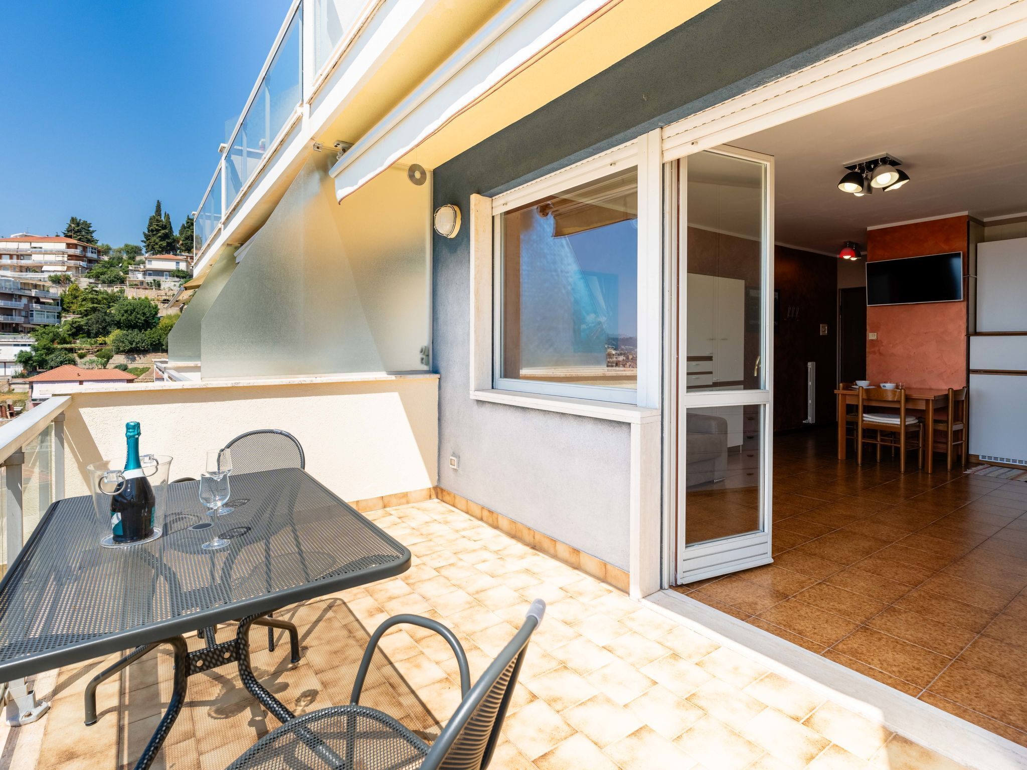 Un balcon avec une table et des chaises, une bouteille de champagne et une vue sur le quartier environnant.