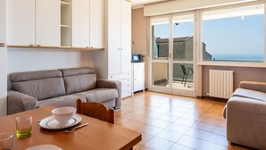 Un salon moderne avec un canapé, une table à manger et une vue sur la mer grâce à de grandes fenêtres.