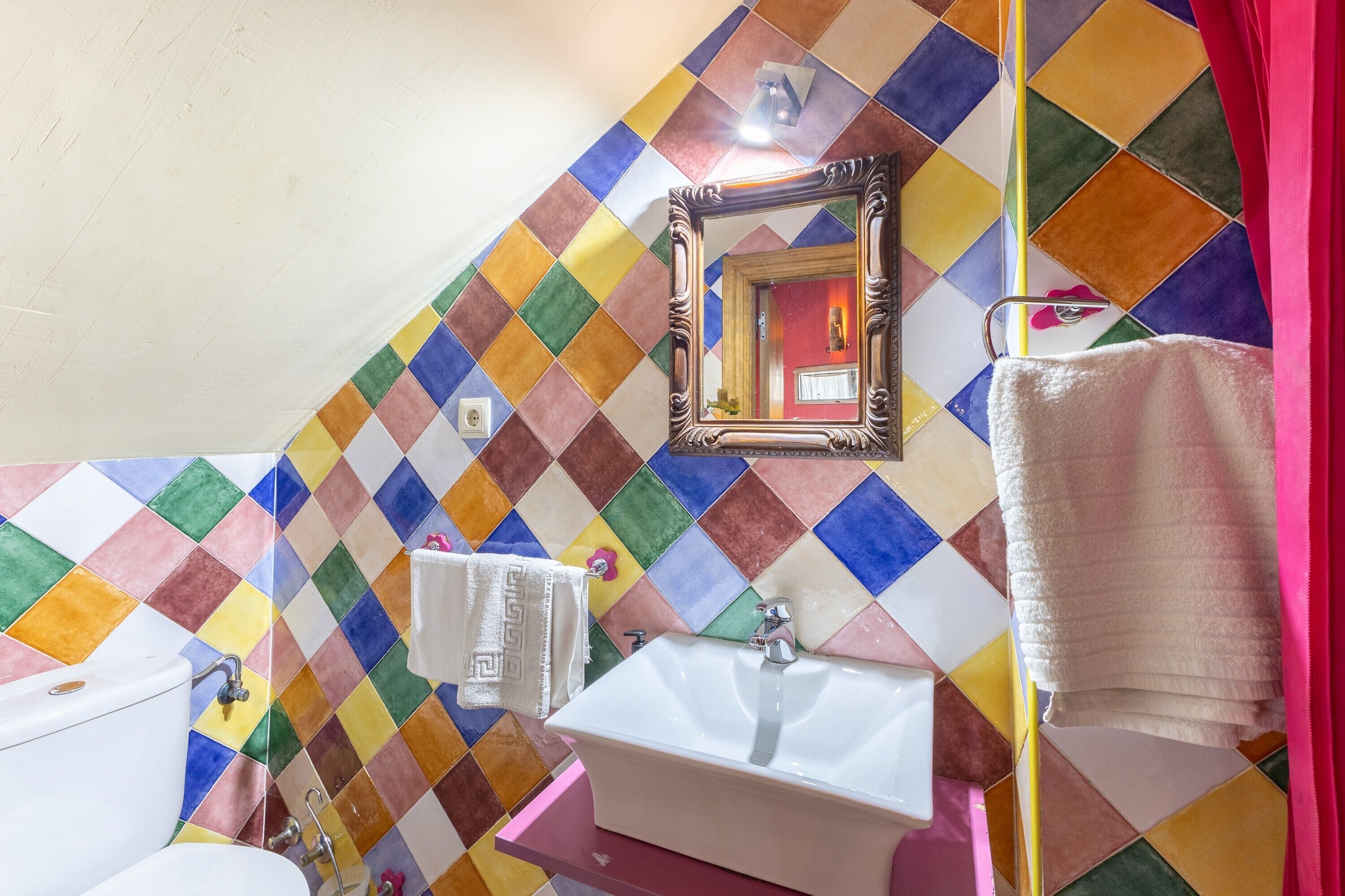 Ein Badezimmer mit Wandfliesen in verschiedenen Farben, einem weißen Waschbecken, einem Spiegel und einem Handtuchhalter.