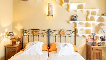 Una cama doble con ropa de cama blanca y naranja, un cabecero de metal y una mesita de noche de madera con una lámpara.