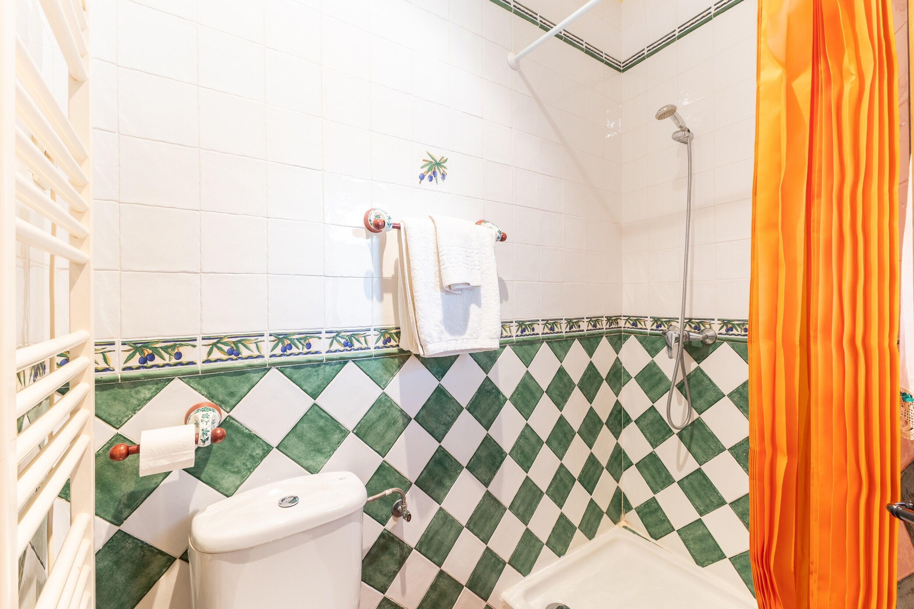 Un baño con inodoro, ducha y pared de azulejos con diseño de cuadros.