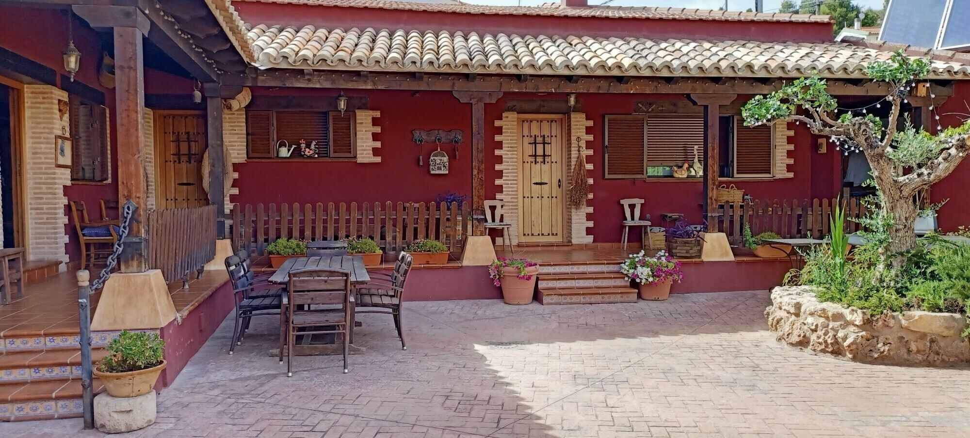 Ein rotes Gebäude mit Ziegeldach, Holztüren und einer Terrasse mit Tisch und Stühlen.