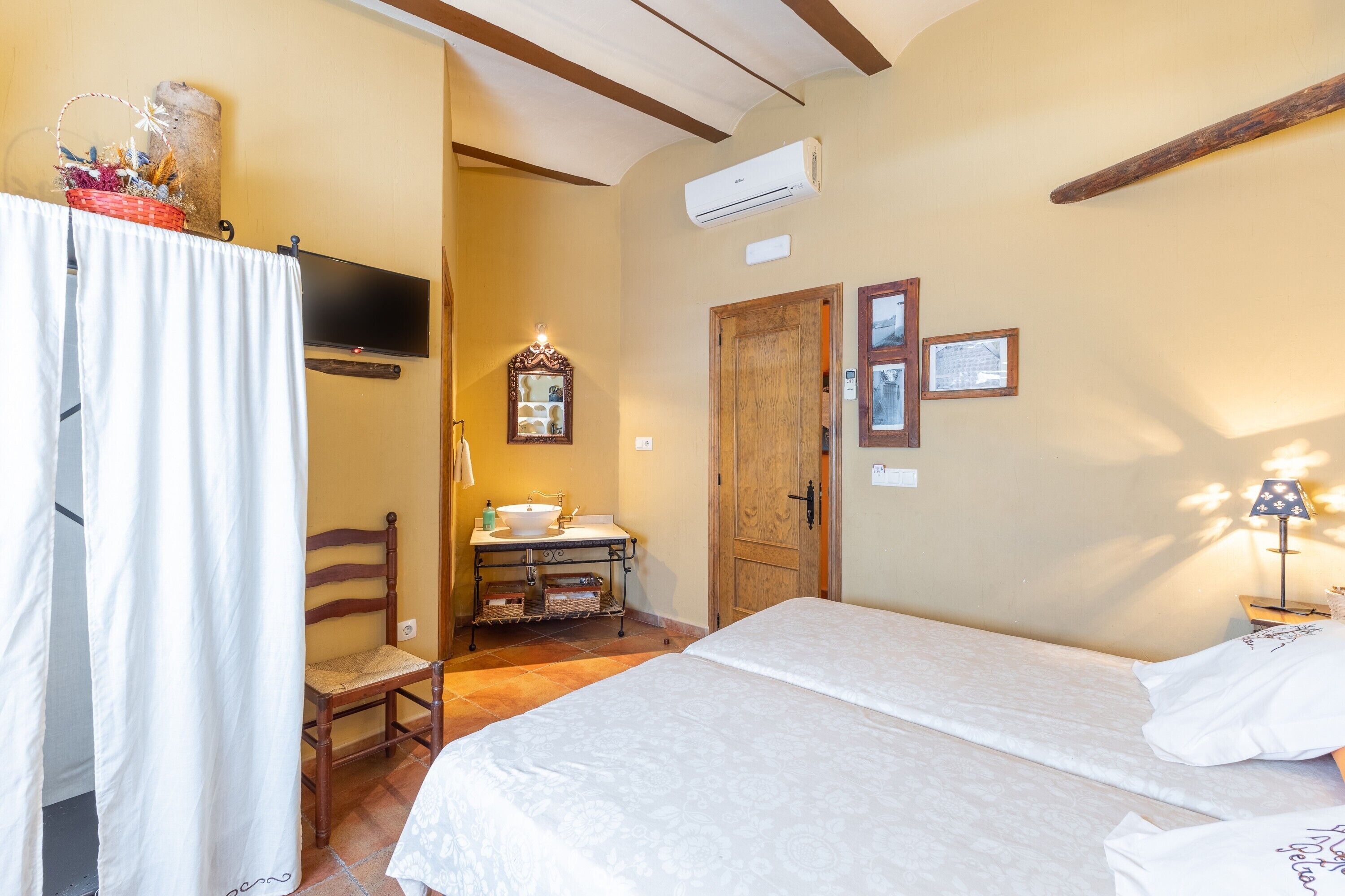 Un dormitorio con cama, una puerta de madera, un espejo, un lavabo y una ventana.