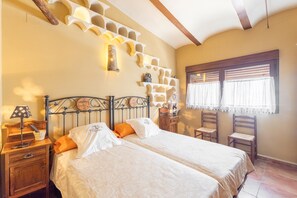 Quarto com duas camas, mesa de cabeceira de madeira, luminária, cadeira e janela com cortinas.