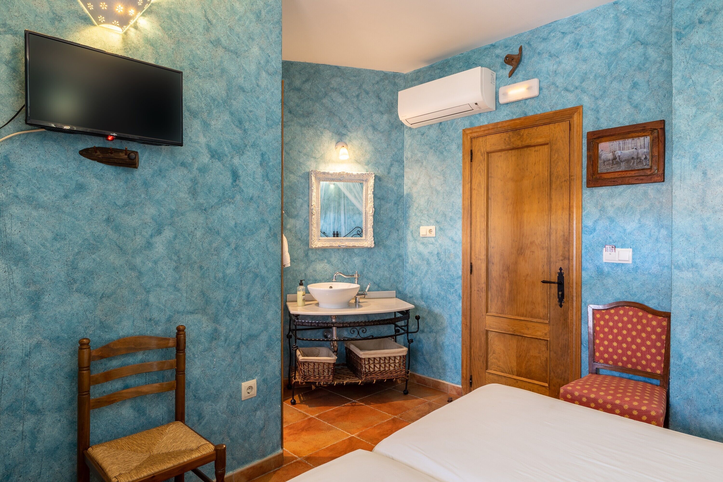 Une chambre avec une télévision, une porte en bois, une salle de bain avec un lavabo et une chaise.