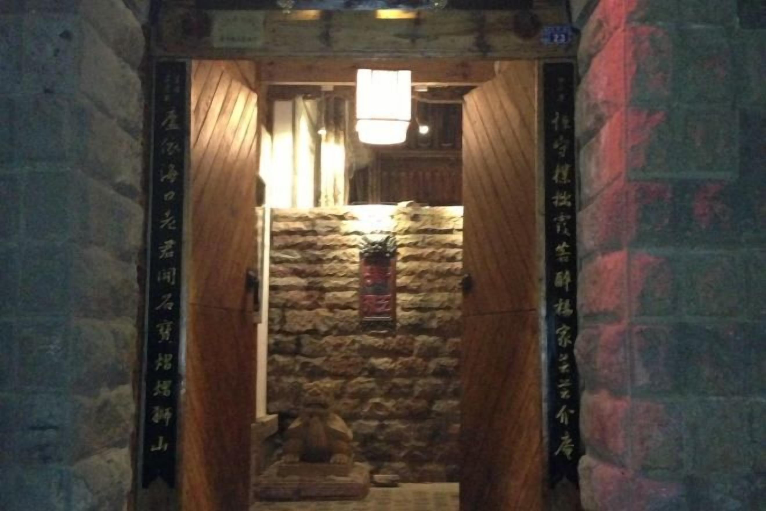A narrow stone corridor with wooden doors and a hanging light fixture.