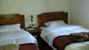 A room with two single beds, each with a wooden headboard, white linens, and a bedside table with a lamp and a book.