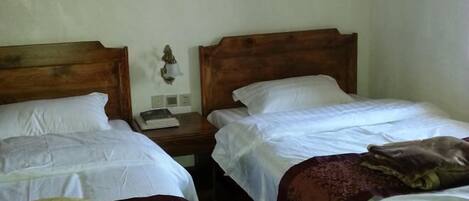 A room with two single beds, each with a wooden headboard, white linens, and a bedside table with a lamp and a book.