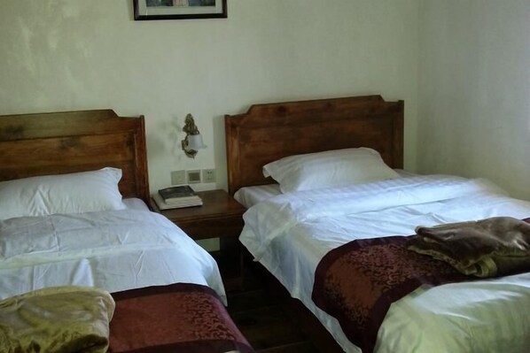 A room with two single beds, each with a wooden headboard, white linens, and a bedside table with a lamp and a book. - Henglu Inn (Jianchuan)