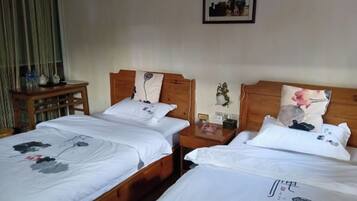 A hotel room with two wooden beds, white bedding, and floral patterns. There is a small wooden table with a lamp and a picture frame on the wall.