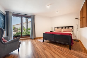 Une chambre à coucher avec un lit, une chaise, une lampe sur pied et une vue à travers une porte vitrée.