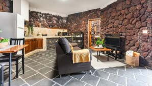 Salón con sofá, televisor y mesa de comedor, cocina con pared de piedra y suelo de piedra.
