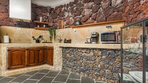 Una cocina con paredes de piedra, armarios de madera, microondas integrado y cafetera.