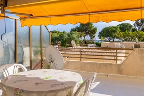 Een terras buiten met een tafel, stoelen en een geel zonnescherm.