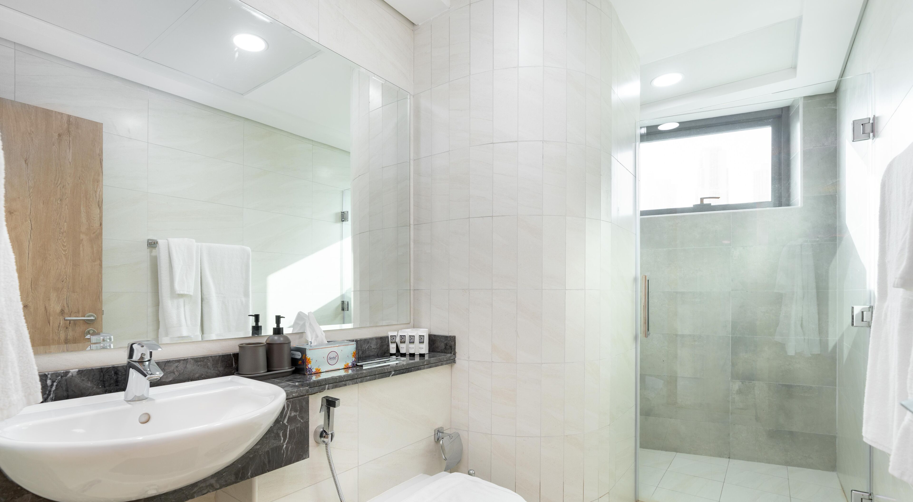 Un baño moderno con lavamanos, espejo y ducha blancos.