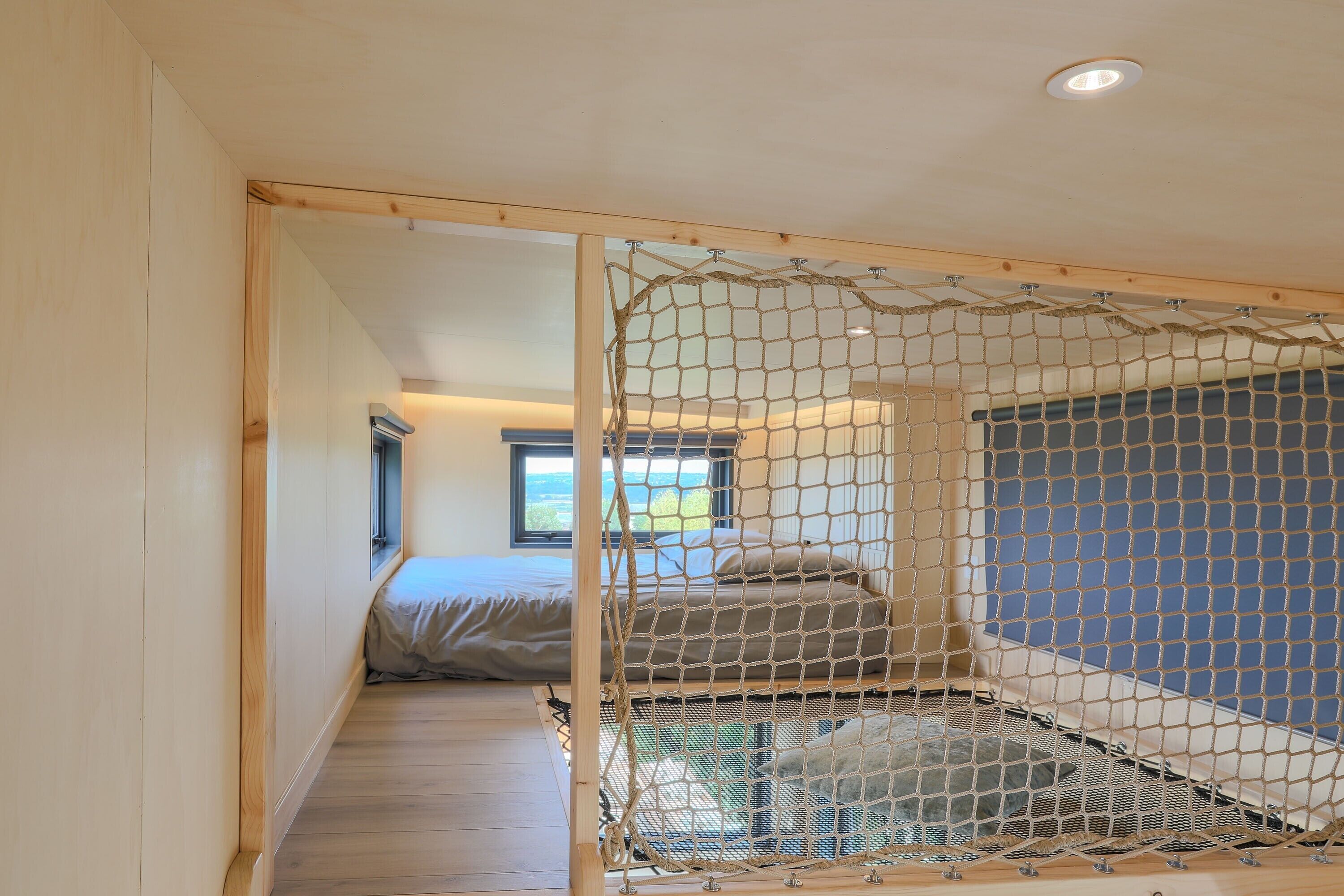Una habitación con piso de madera, una cama con colchón gris y un toldo de mosquitero.