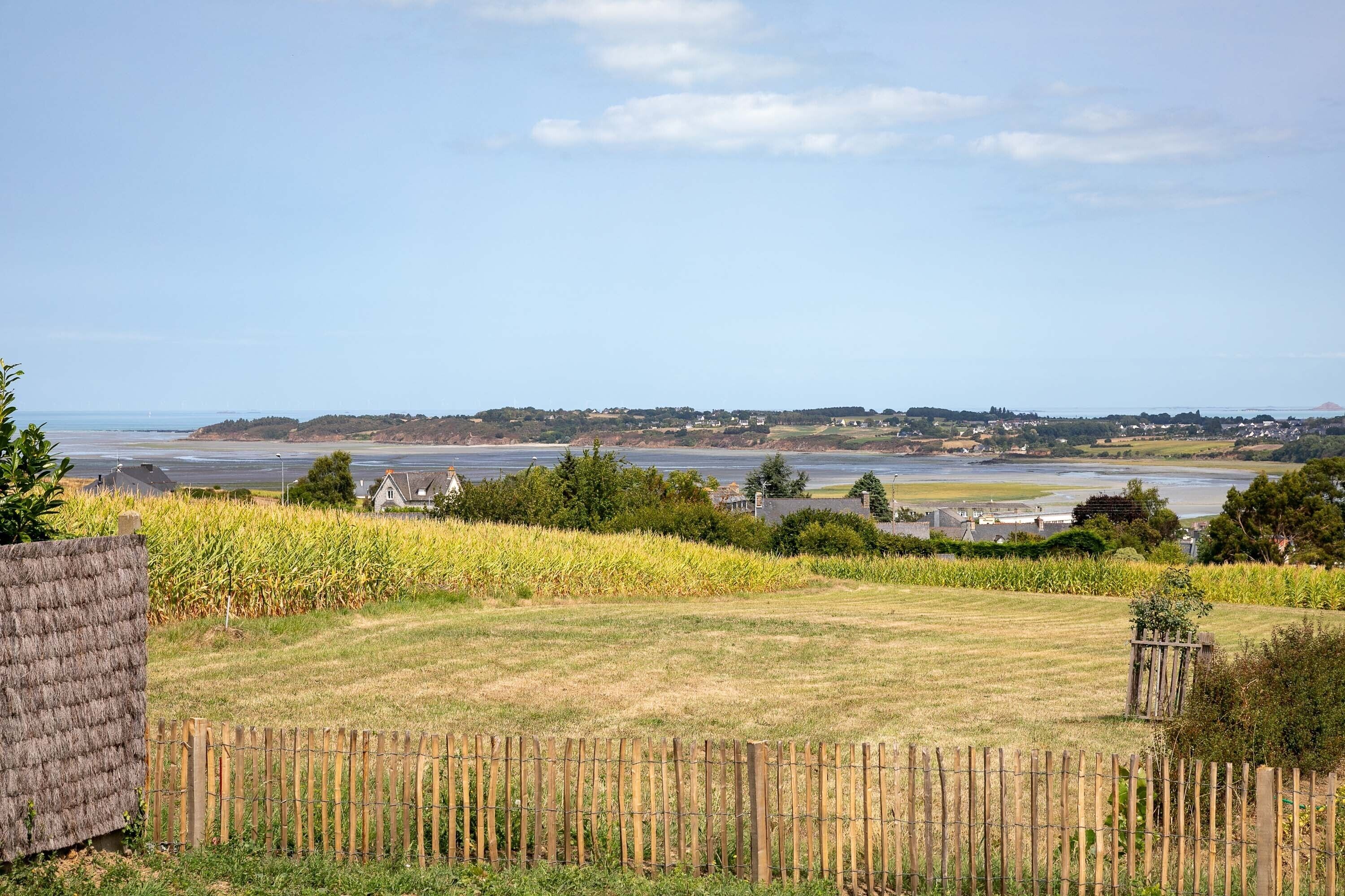 A rural landscape with a field, a wooden fence, and a distant view of a body of water and buildings.