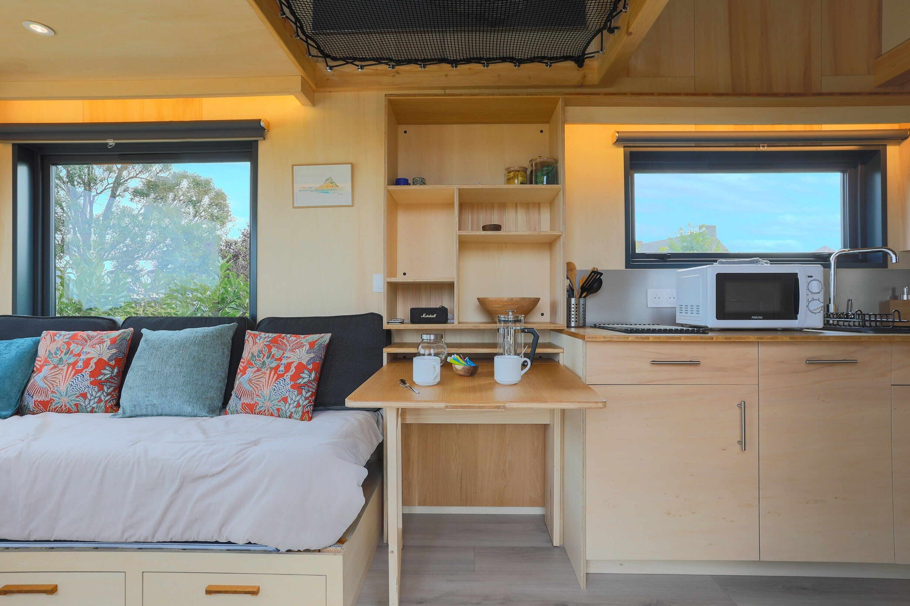 A compact bedroom with a bed, a small kitchenette with a microwave, and a window with a view of trees.