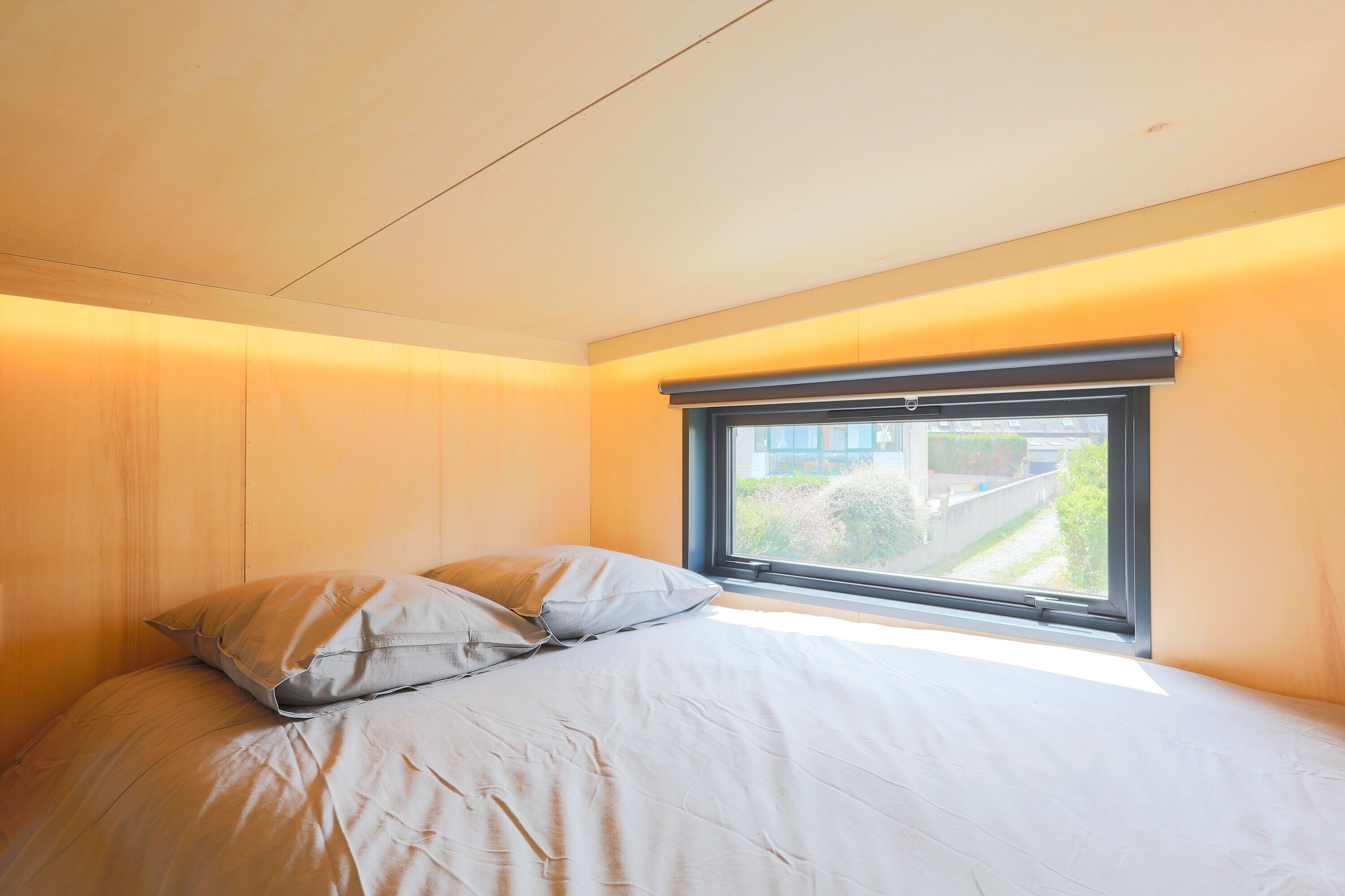 A bedroom with a bed, pillows, a window, and a view of greenery outside.