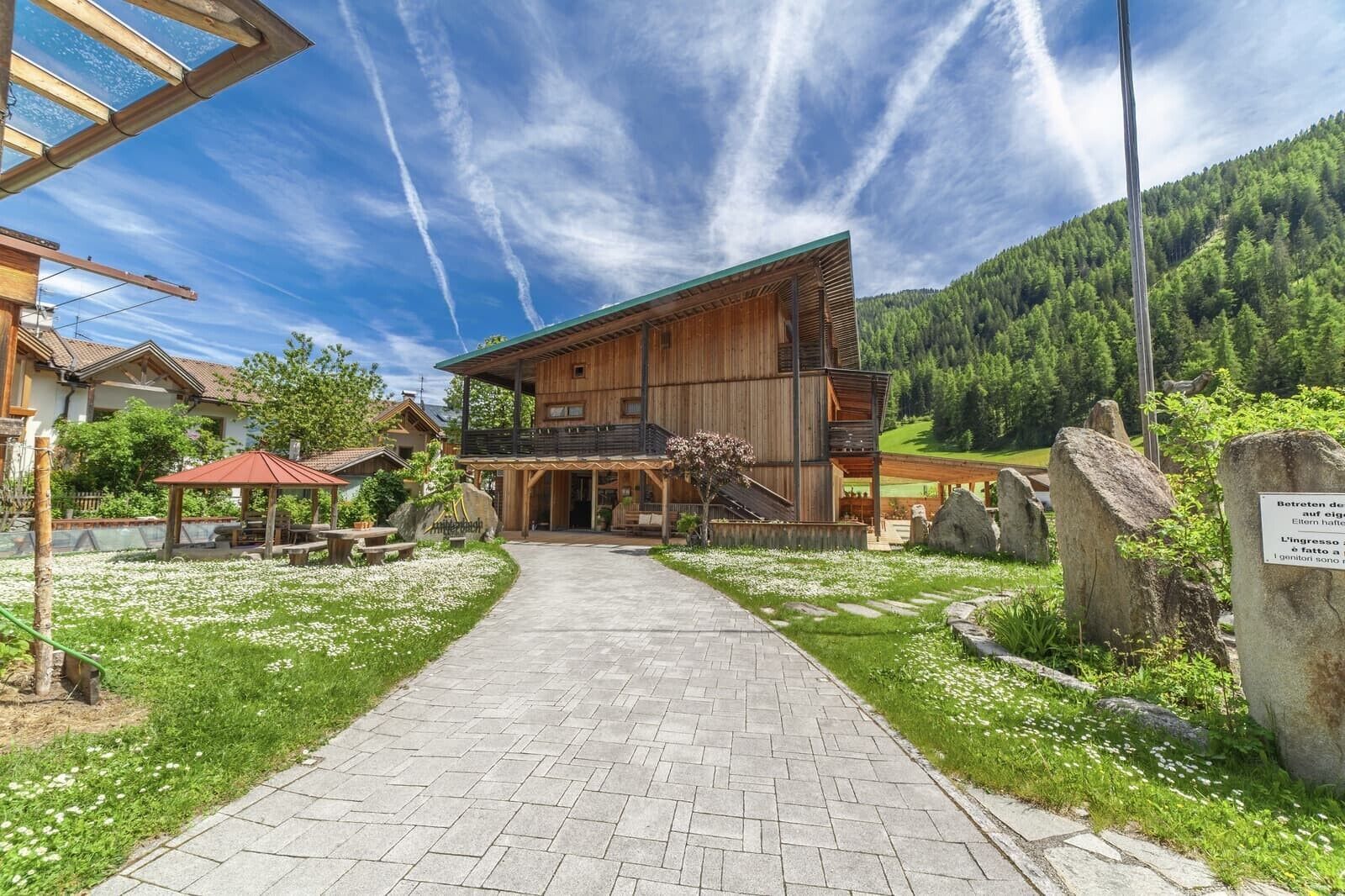 Un edificio in legno con un balcone, un vialetto lastricato e montagne sullo sfondo.