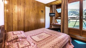 A wooden-paneled room with a bed, a television, and a view of a mountainous landscape.