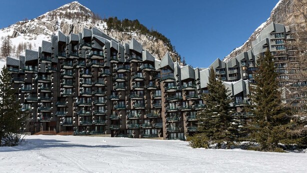 A modern hotel with multiple balconies, set against a snowy mountain backdrop.