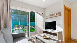 Una sala moderna con un sofá, una mesa de centro, un televisor de pantalla plana y un ventanal corredero que da a un espacio exterior.