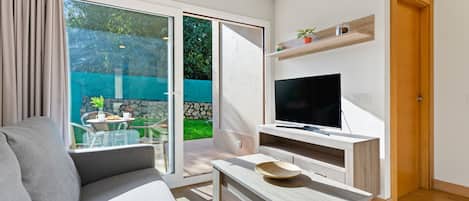 A modern living room with a sofa, a coffee table, a flat-screen TV, and a sliding glass door leading to an outdoor area.