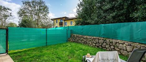 A backyard with a green fence, a stone wall, and a house in the background.
