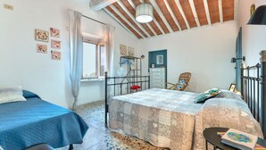 Een slaapkamer met twee bedden, een raam met gordijnen, een ventilator, een dressoir en een stoel.