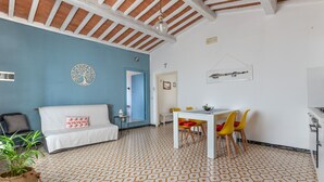 Een kamer met een patroon vloer, een witte bank met een rood kussen, een eettafel met gele stoelen, en een hanglamp.