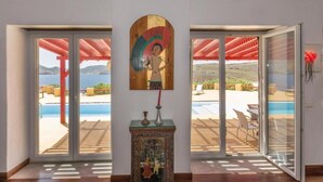 A room with a view of a pool and outdoor seating, a wooden sculpture, and a large window. - Villa 'Agios Sostis Mykonos' with Sea View, Wi-Fi and Air Conditioning (Mýkonos City)