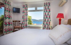 Una habitación de hotel con una cama, una silla, un televisor, una lámpara y vistas al mar.